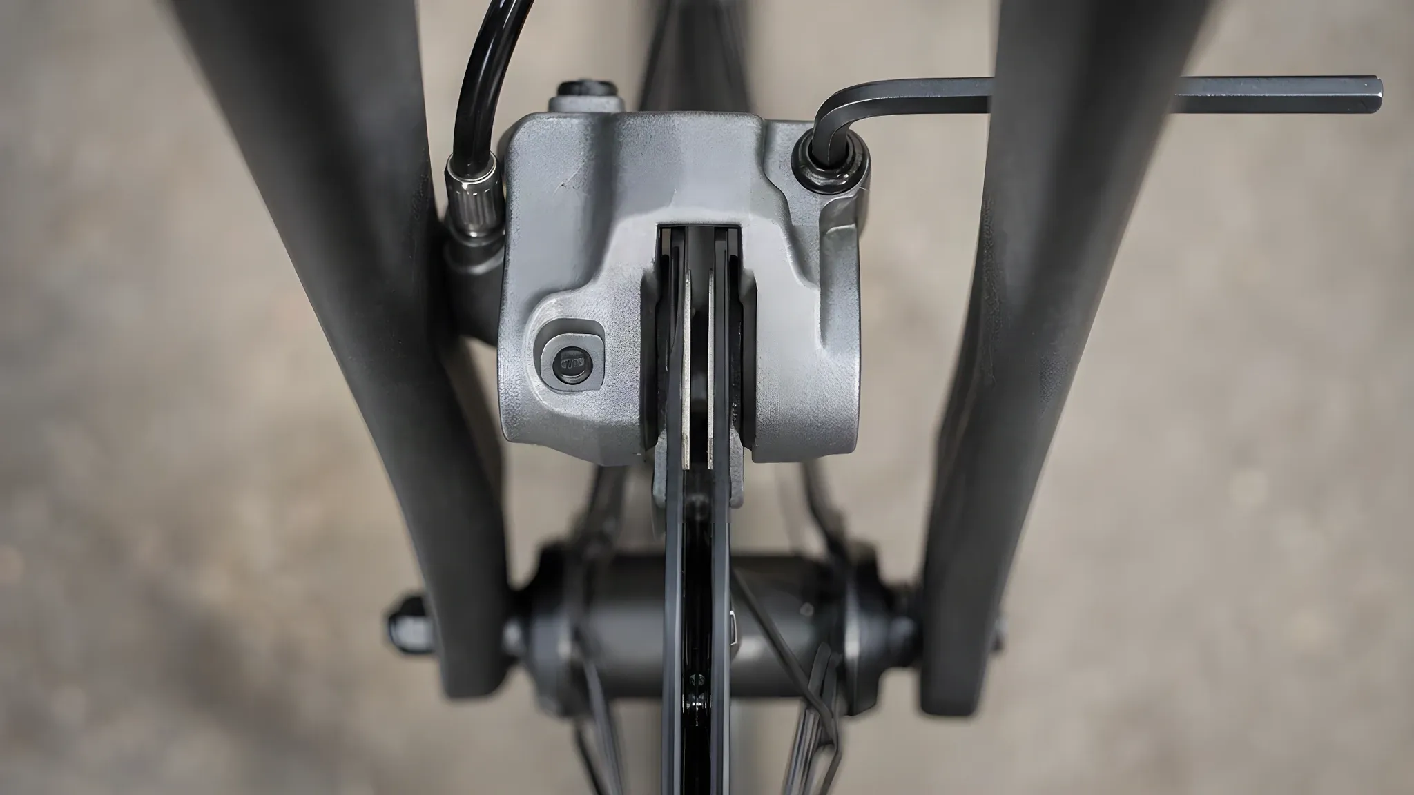 Looking down through a hydraulic disc brake caliper after centring: the rotor sits in the middle of the slot with an even gap each side, a 5 mm Allen key in one mounting bolt