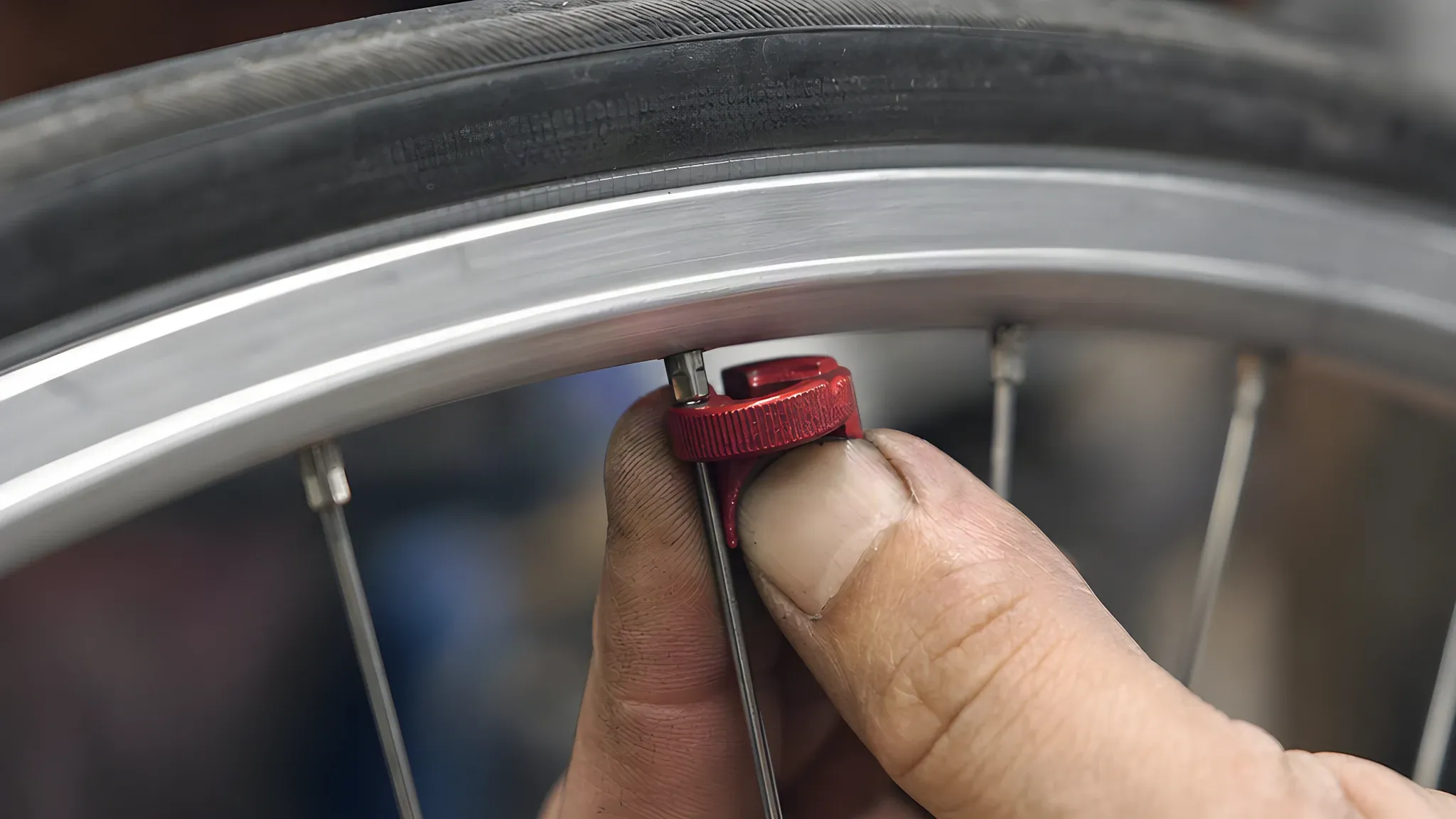 Hand turning a spoke nipple with a red spoke key fitted on the nipple flats just inside an aluminium rim